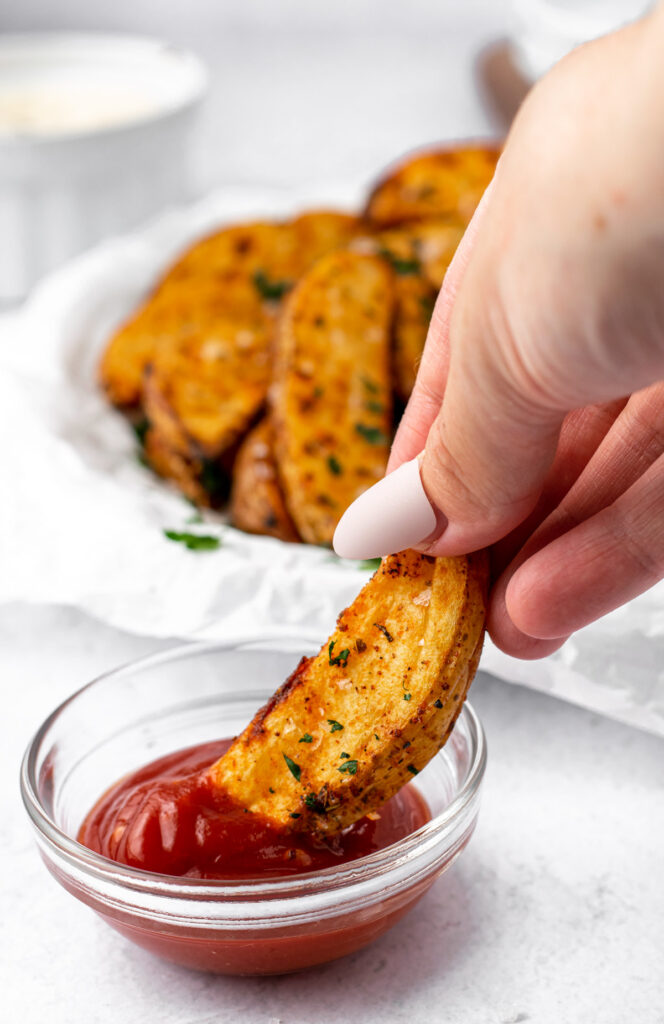 potato wedge being dipped in ketchup