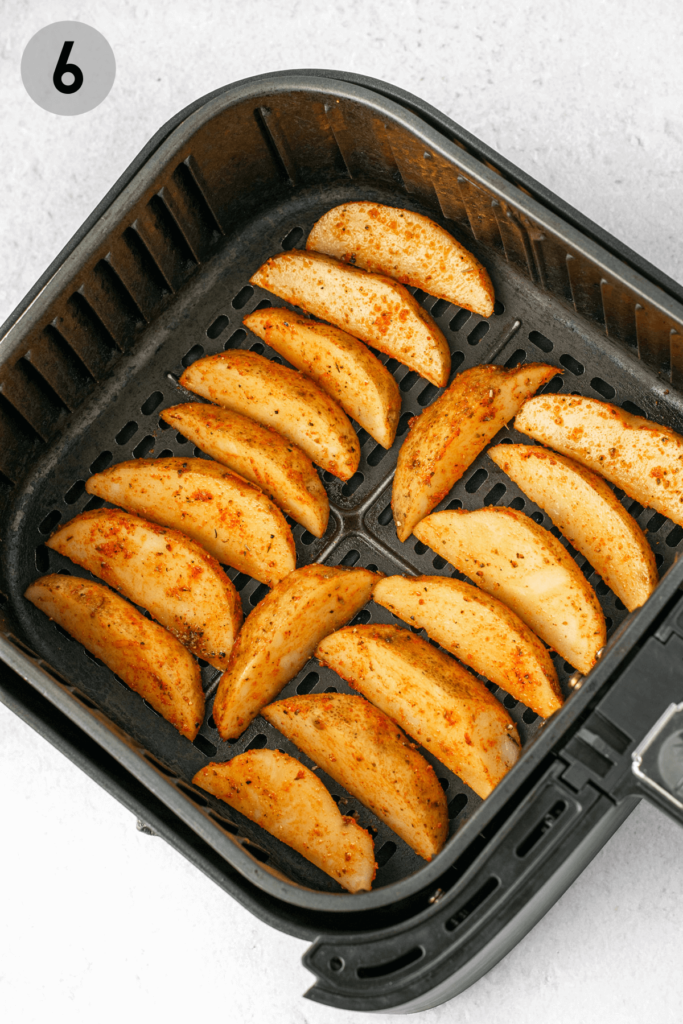 potato wedges lined up in an air fryer basket to be fried
