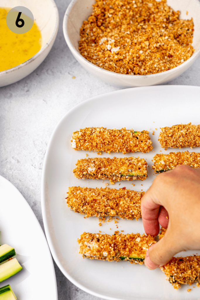 hand placing a breaded zucchini fry onto a plate