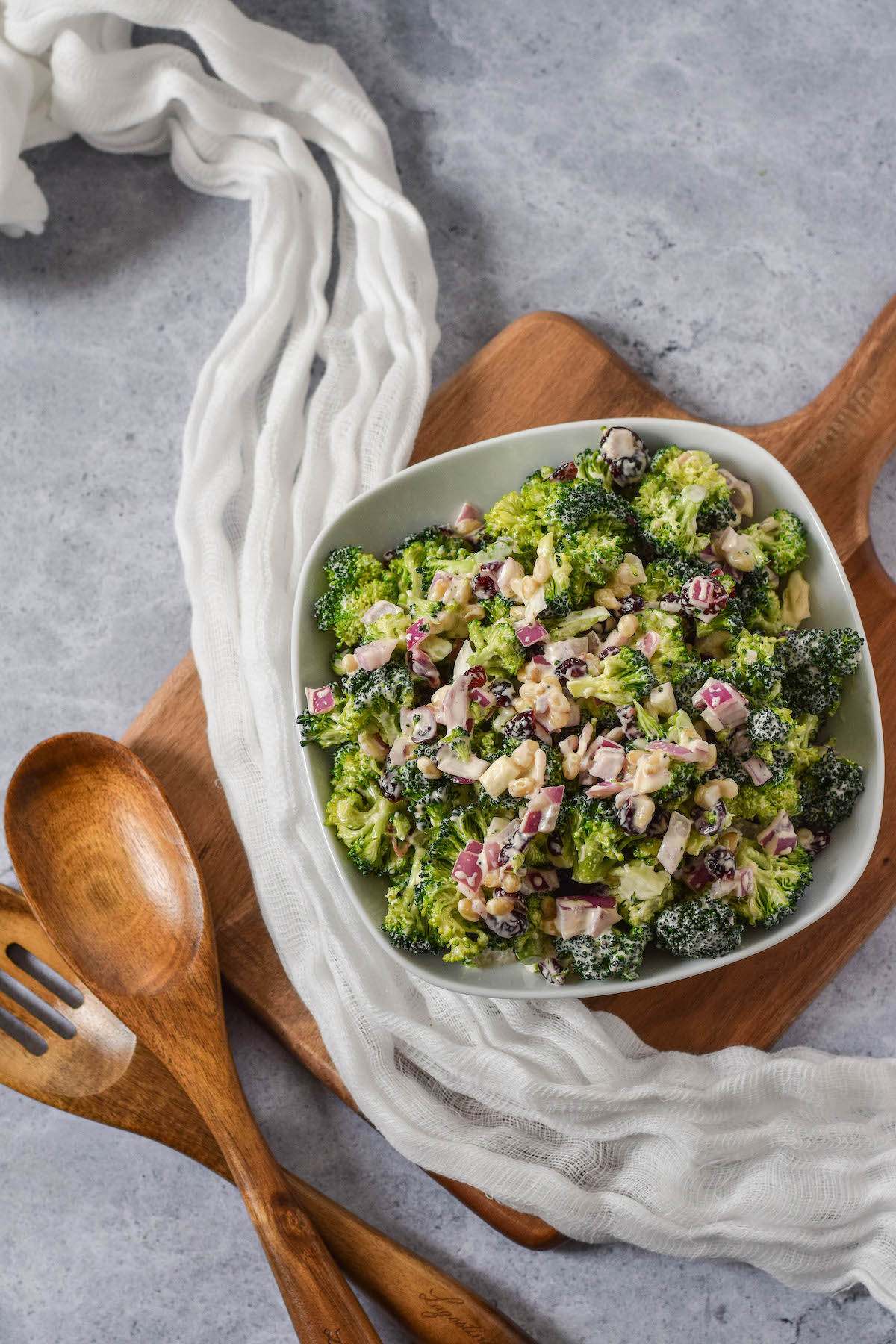 top view of broccoli salad in a white bowl on a wooden cutting board