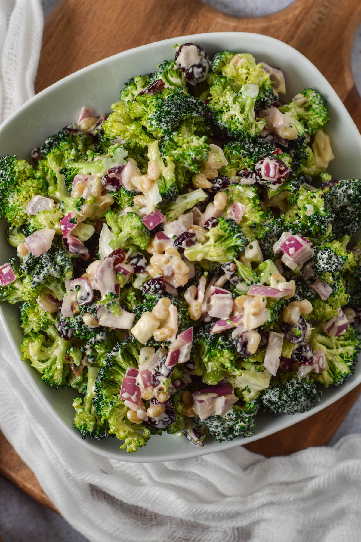 top view of broccoli salad in a white bowl on a wooden cutting board