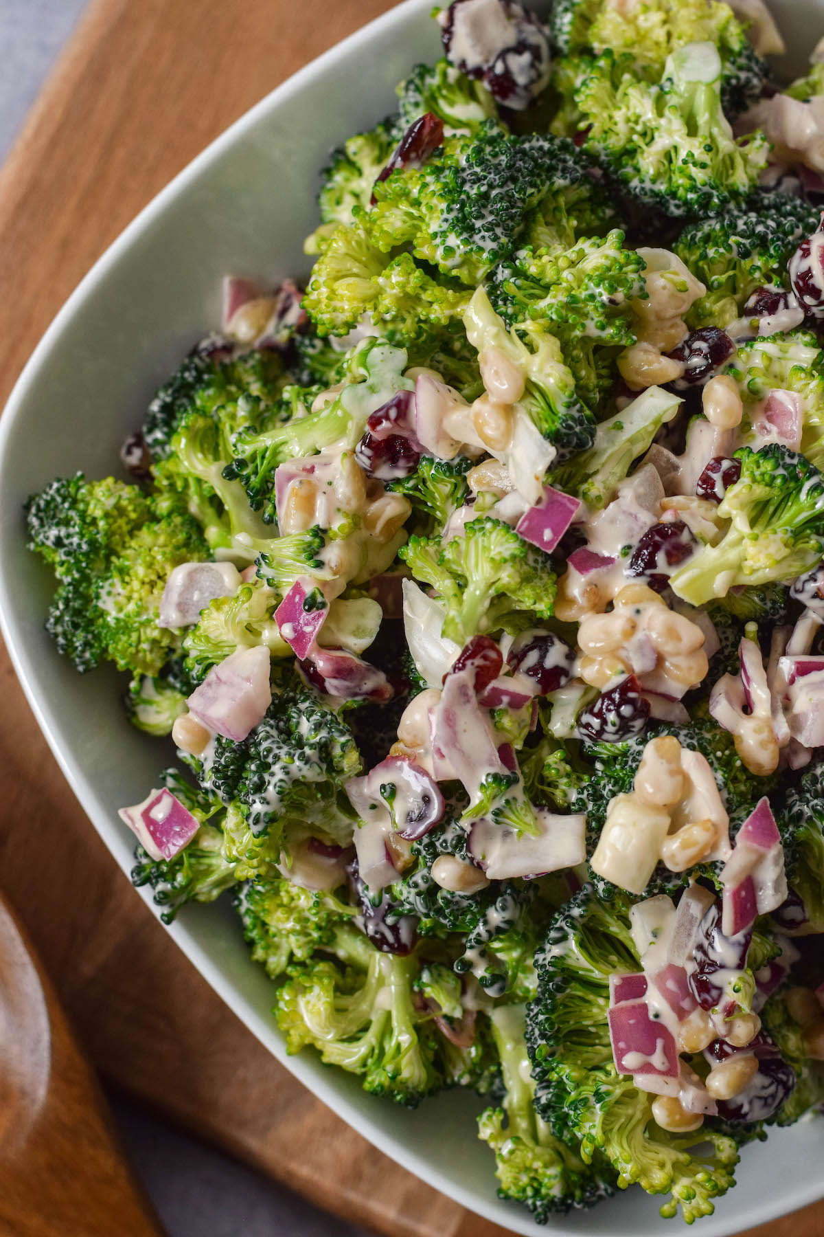 close up of broccoli salad in a white bowl on a wooden cutting board