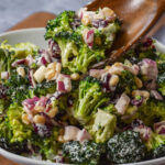 close up of broccoli salad being scooped with a wooden spoon