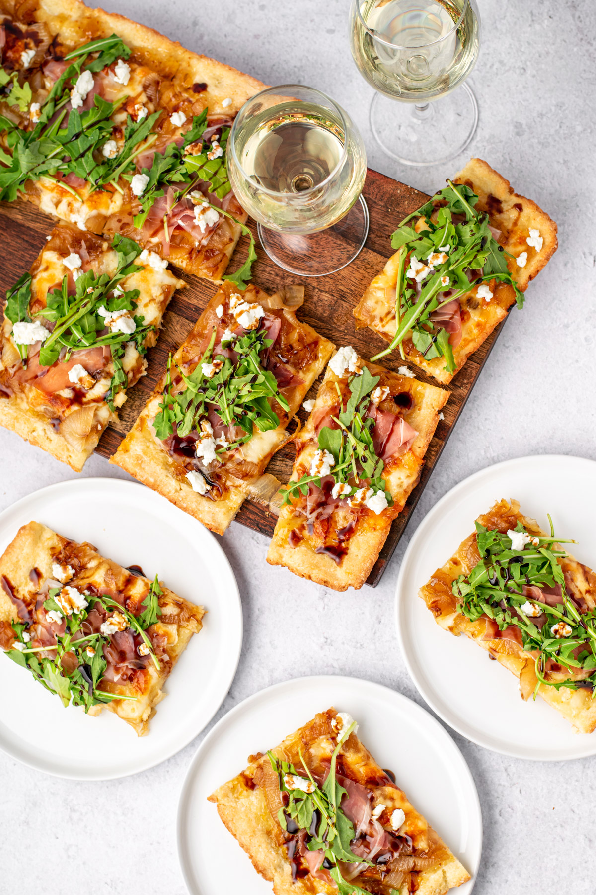 top view of pizza slices on a wood board, plates, and wine glasses