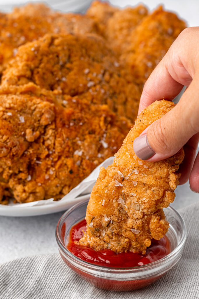 dipping a gluten-free fried chicken tender in ketchup