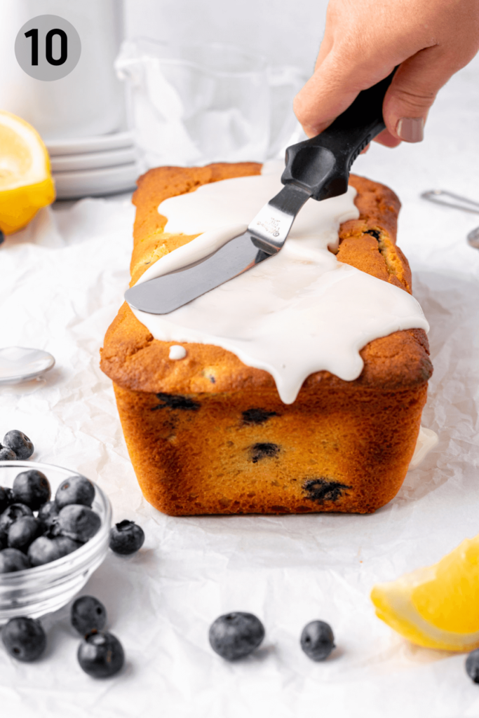 spreading glaze with a spatula on top of lemon blueberry loaf