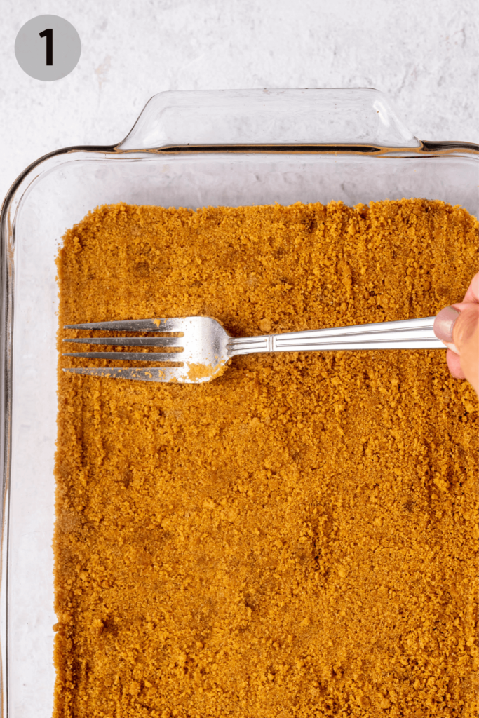 fork pressing graham cracker crumbs into a glass pan