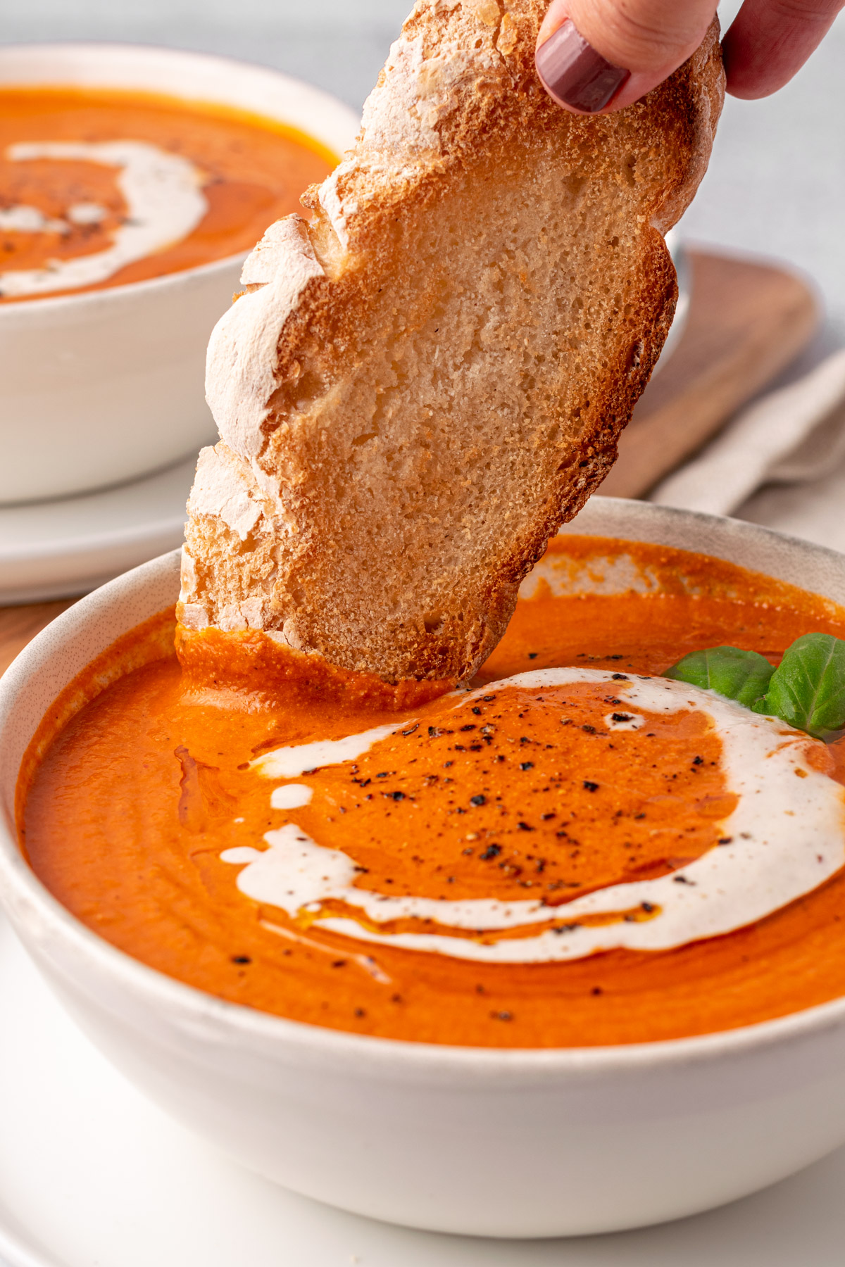 a piece of bread being dunked into a bowl of tomato soup