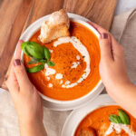 hands grabbing a bowl of gluten free tomato soup