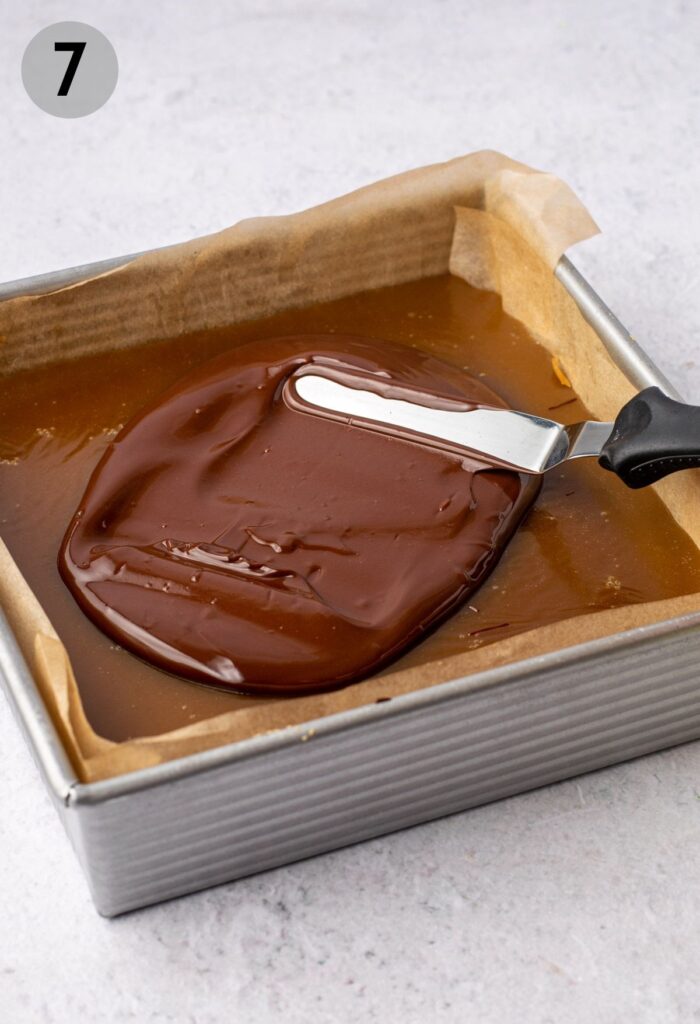 spatula spreading chocolate layer on millionaire shortbreads