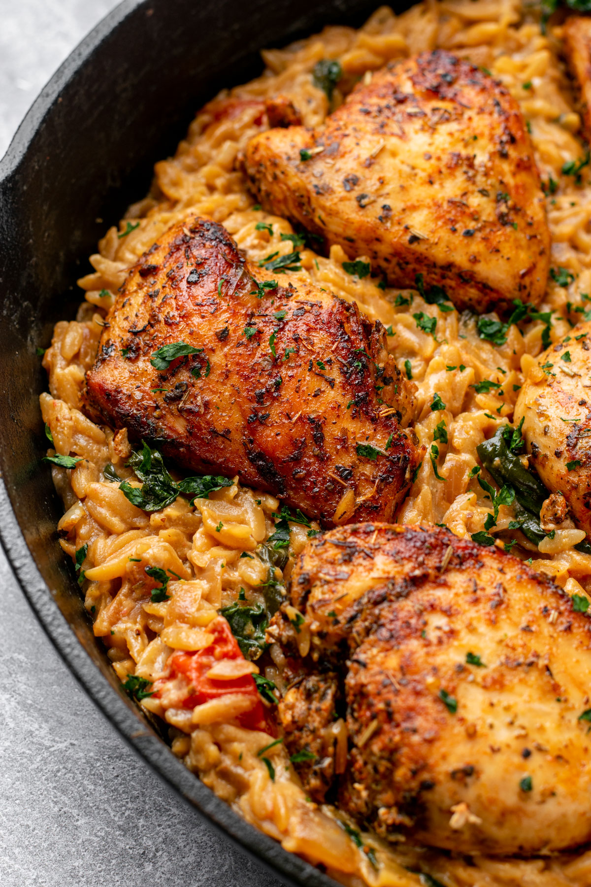 close up of tuscan chicken and orzo in a cast iron skillet