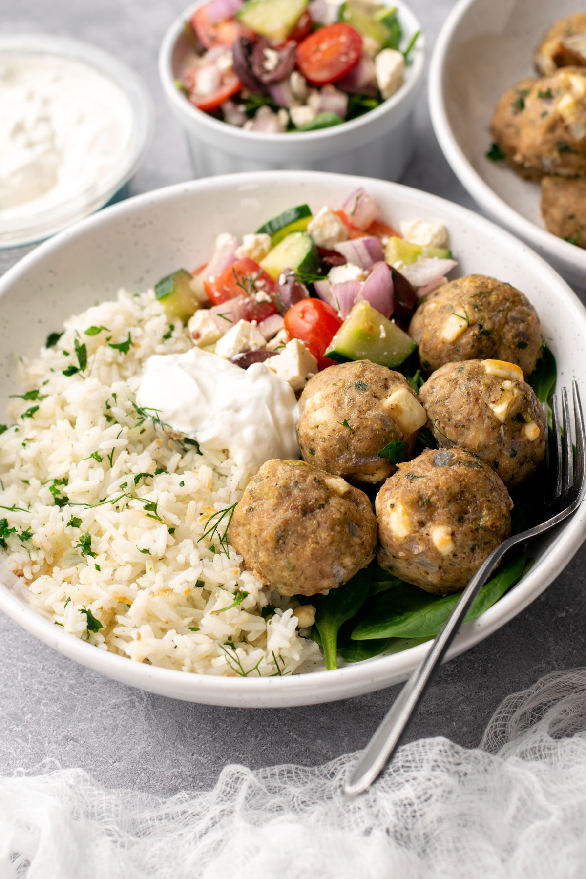bowl with rice, spinach, greek salad, tzatziki, and greek chicken meatballs