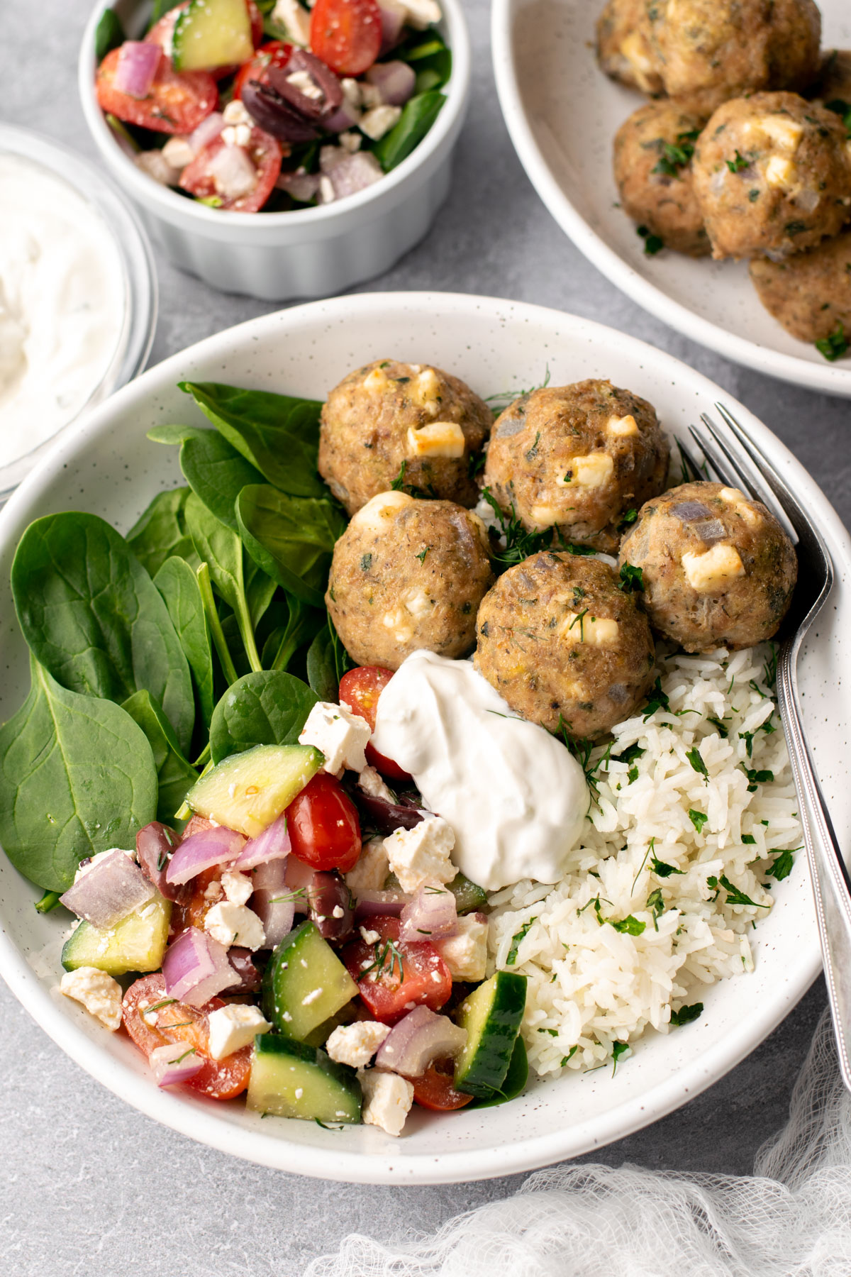 bowl with rice, spinach, greek salad, tzatziki, and greek chicken meatballs