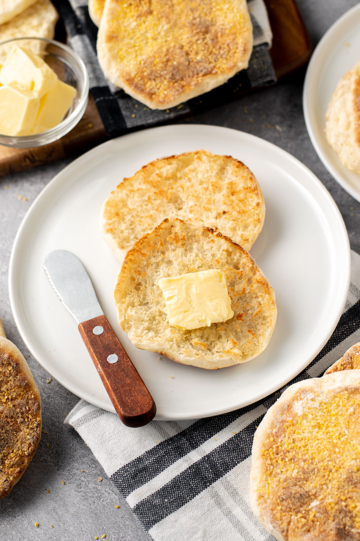 toasted english muffin on a plate with a square of butter and more english muffins around