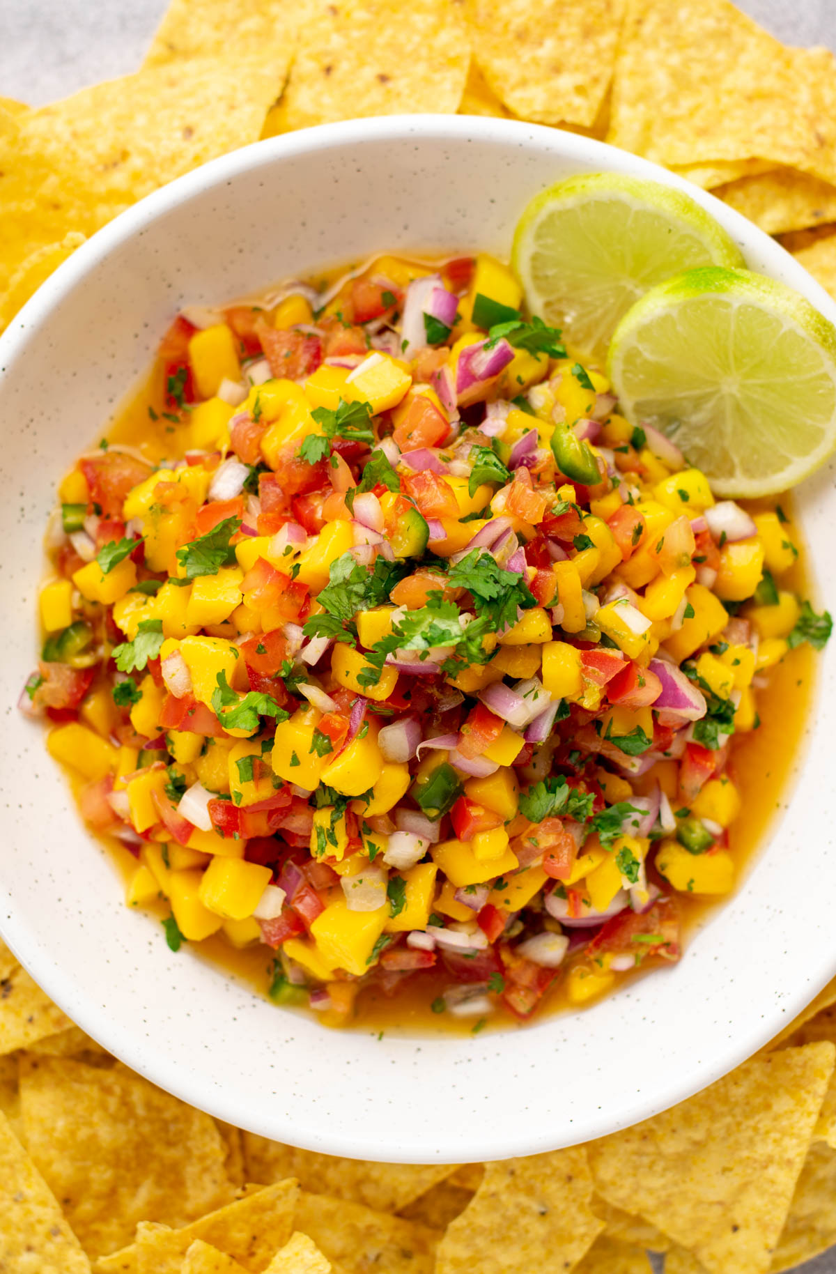 top view of mango pico de gallo with 2 round lime slices in a white bowl