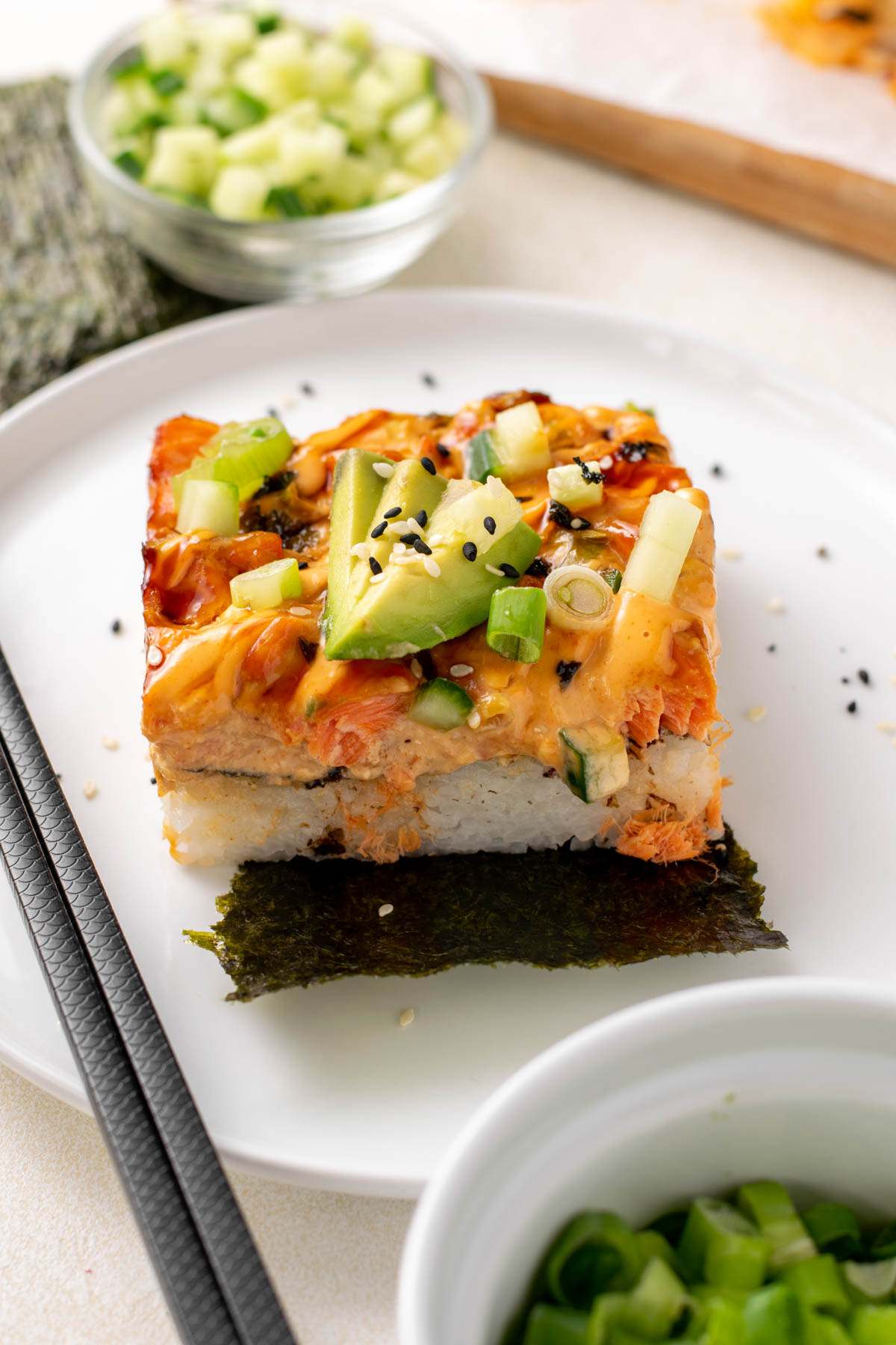 a slice of salmon sushi bake on a white plate with chopsticks.