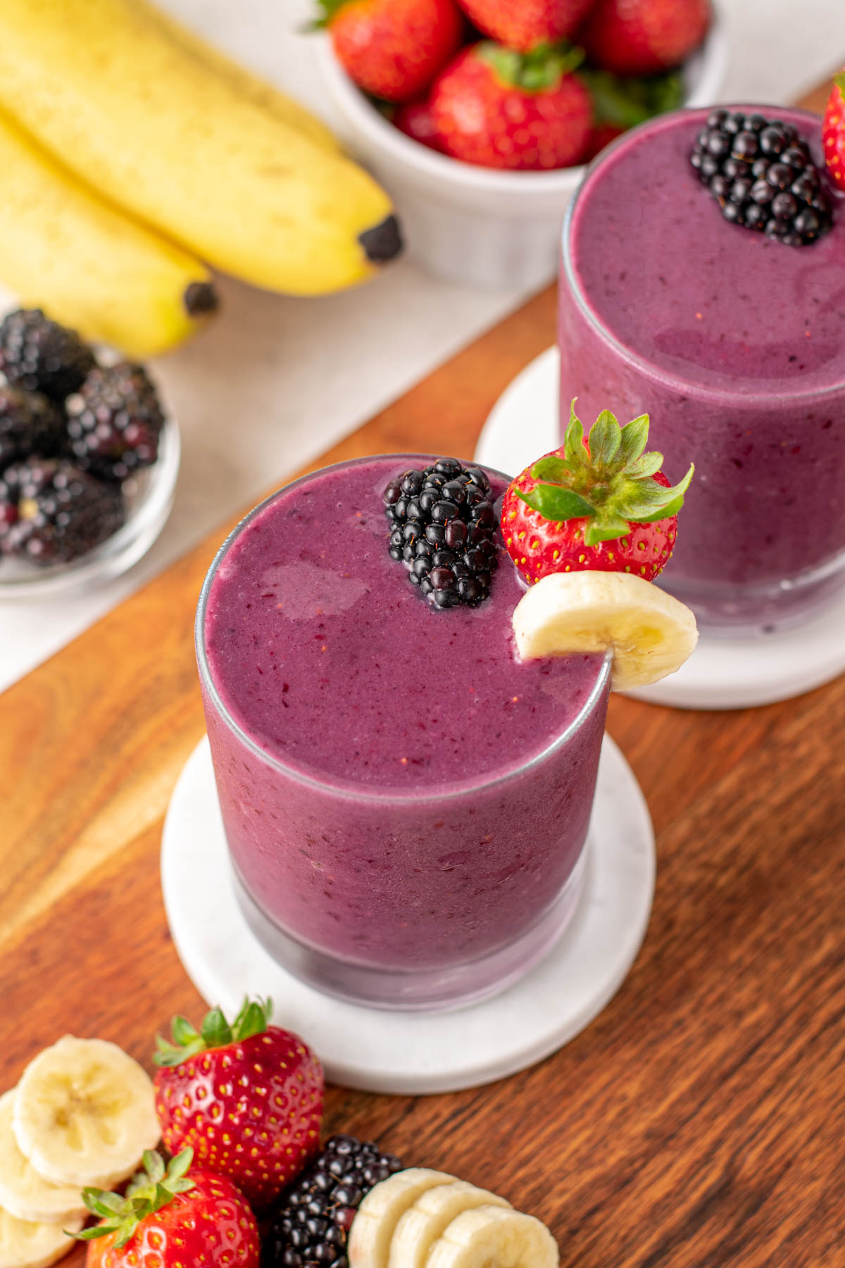 blackberry strawberry banana smoothie with berries on top on a wood board.