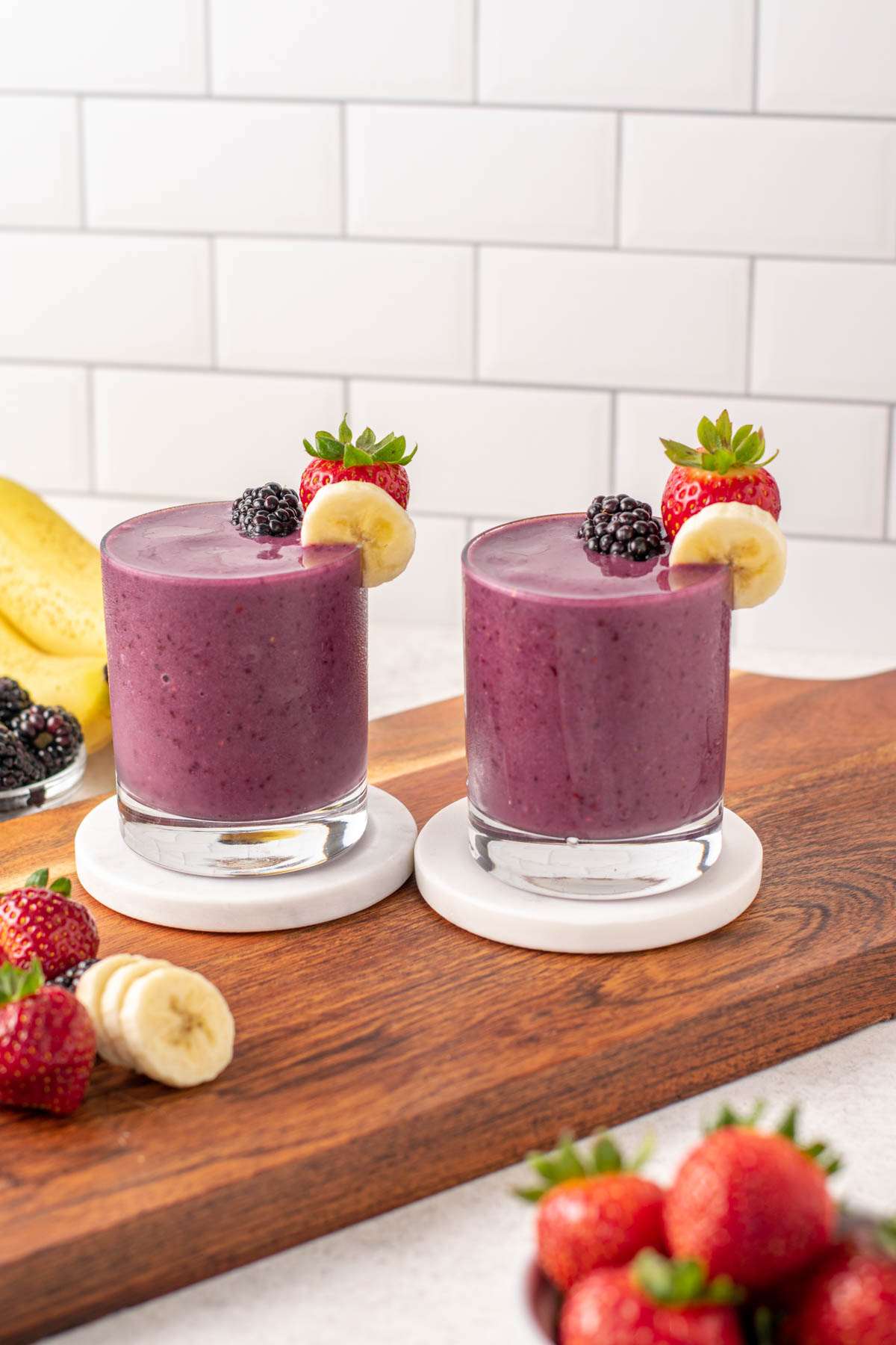 blackberry strawberry banana smoothies in 2 small glasses on a wood board.