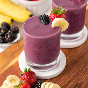 blackberry strawberry banana smoothie in a glass with berries on top.