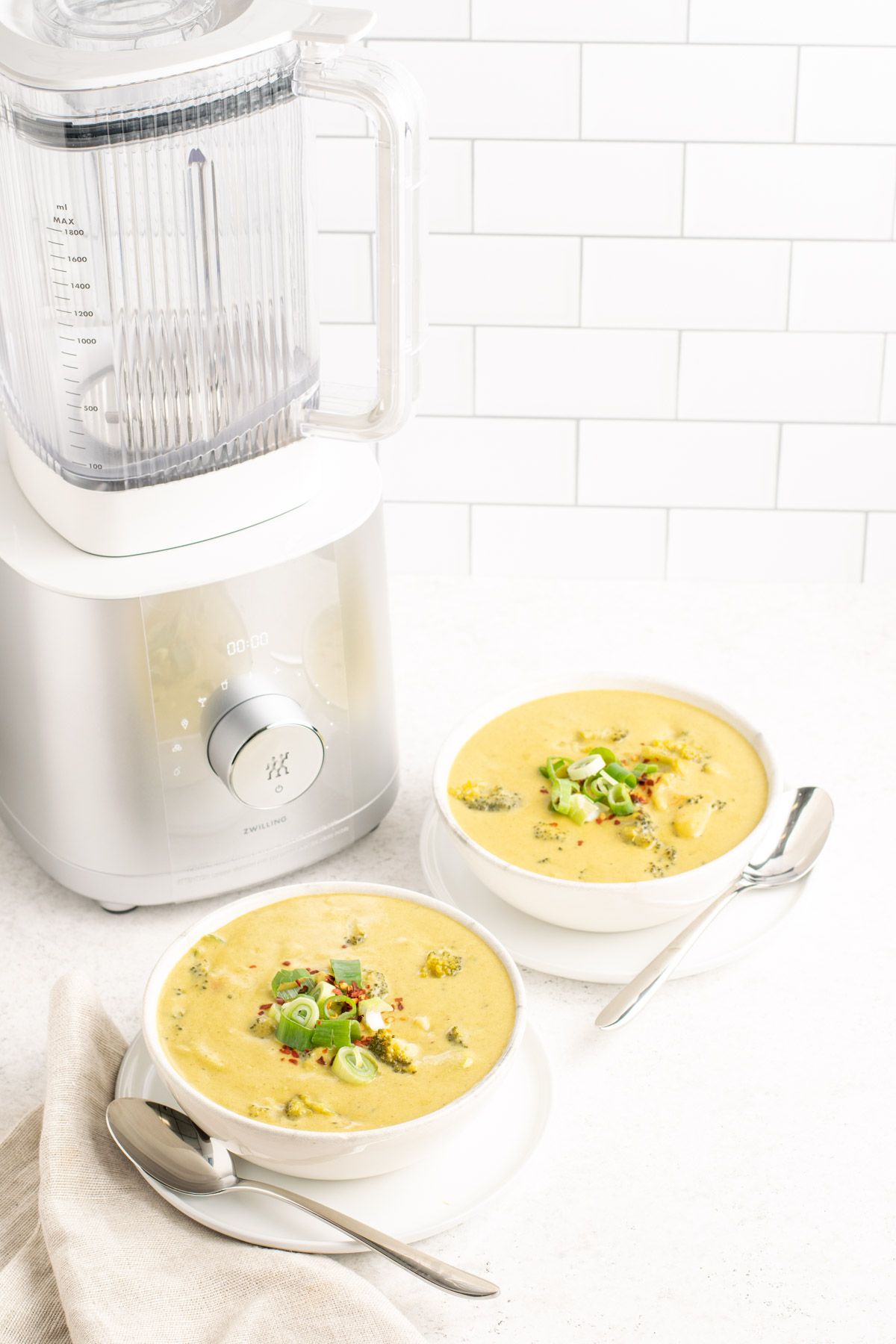 two bowls of dairy free broccoli cheddar soup beside the zwilling ENFINIGY powder blender.