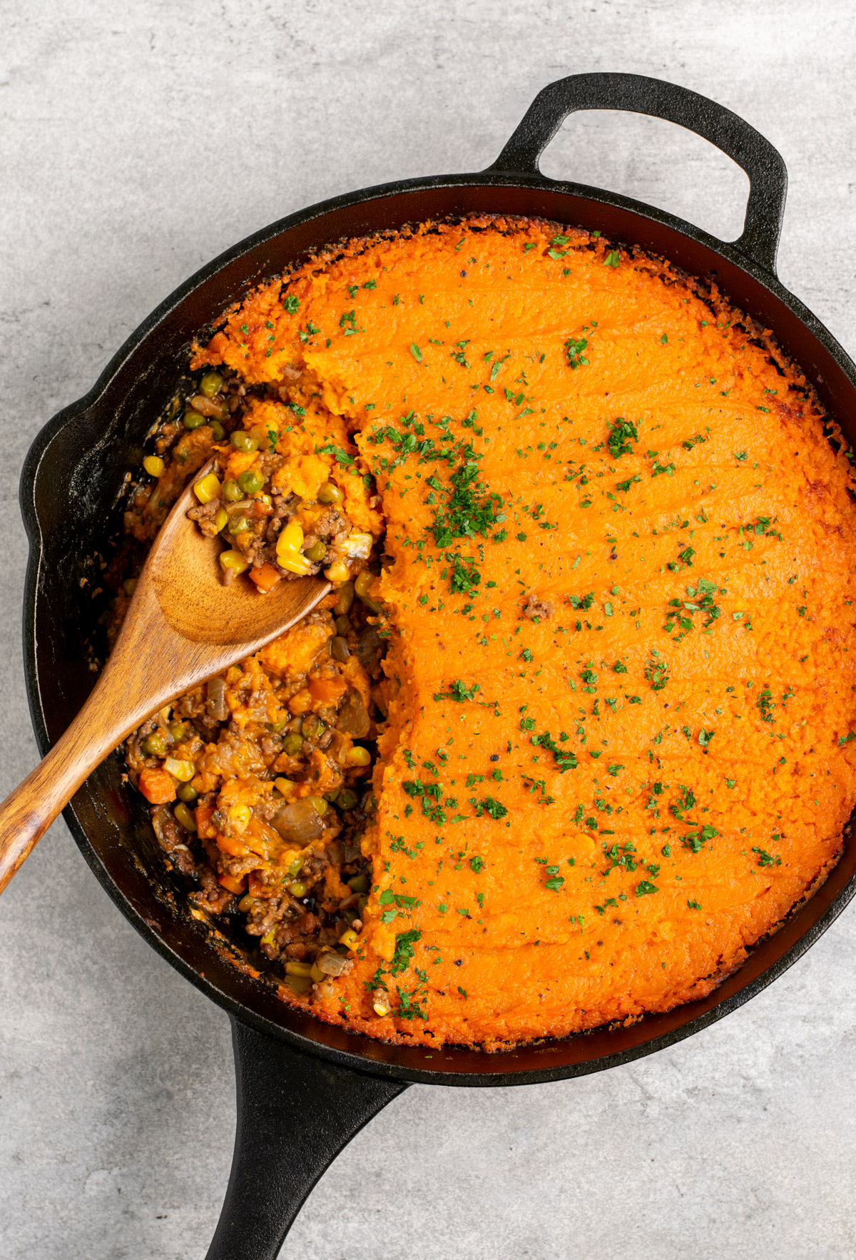 top view of wooden spoon scooping sweet potato shepherd's pie from a cast iron skillet.